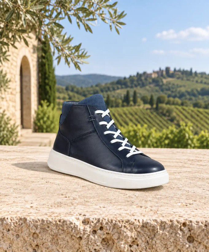 نمای داخلی نیمبوت سرمهای با زیپ تیره کنار ساق، بندهای سفید و زیره سفید روی سطح سنگیelmashoes